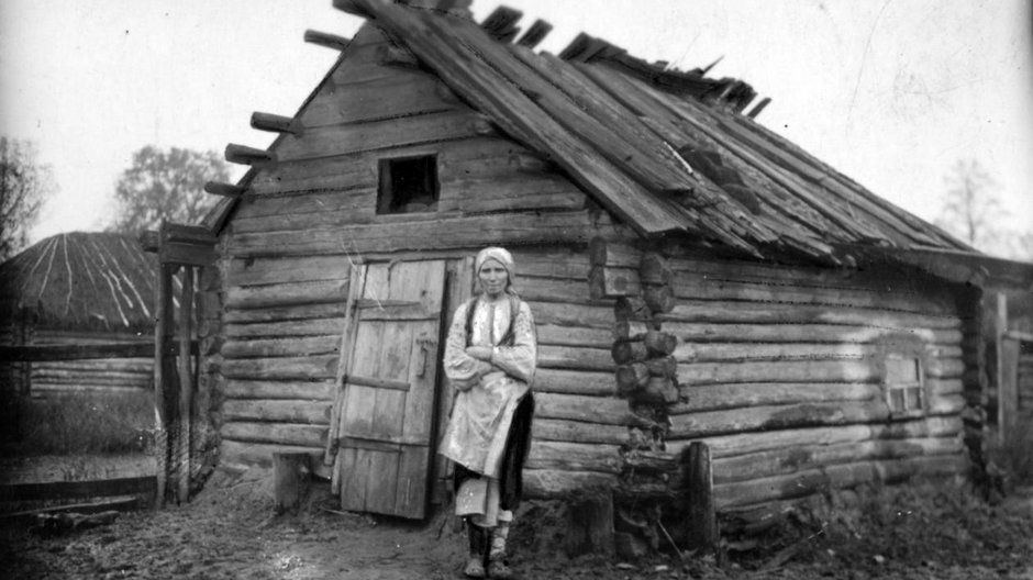 Kobieta z powiatu sarneńskiego stojąca przed swoją chatą.