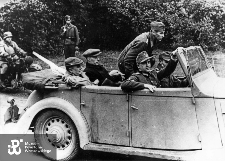 Na tylnym siedzeniu samochodu (prawdopodobnie jest to Polski Fiat 518 Mazur) od lewej ppłk Zygmunt Dobrowolski "Zyndram" (1897–1972), a obok niego – w ciemnym płaszczu – por. Alfred Korczyński "Sas" (1904–1994). Zdjęcie zrobione 28 września lub 2 października 1944 r. na podjeździe przed dworem Reicherów w Ożarowie Mazowieckim