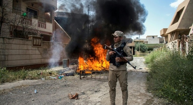 A militiaman stands guard as a family returning to Iraq's main Christian town Qaraqosh following its recapture from the Islamic State group makes a bonfire on May 5, 2017 of damaged furniture and rubbish that the jihadists left behind