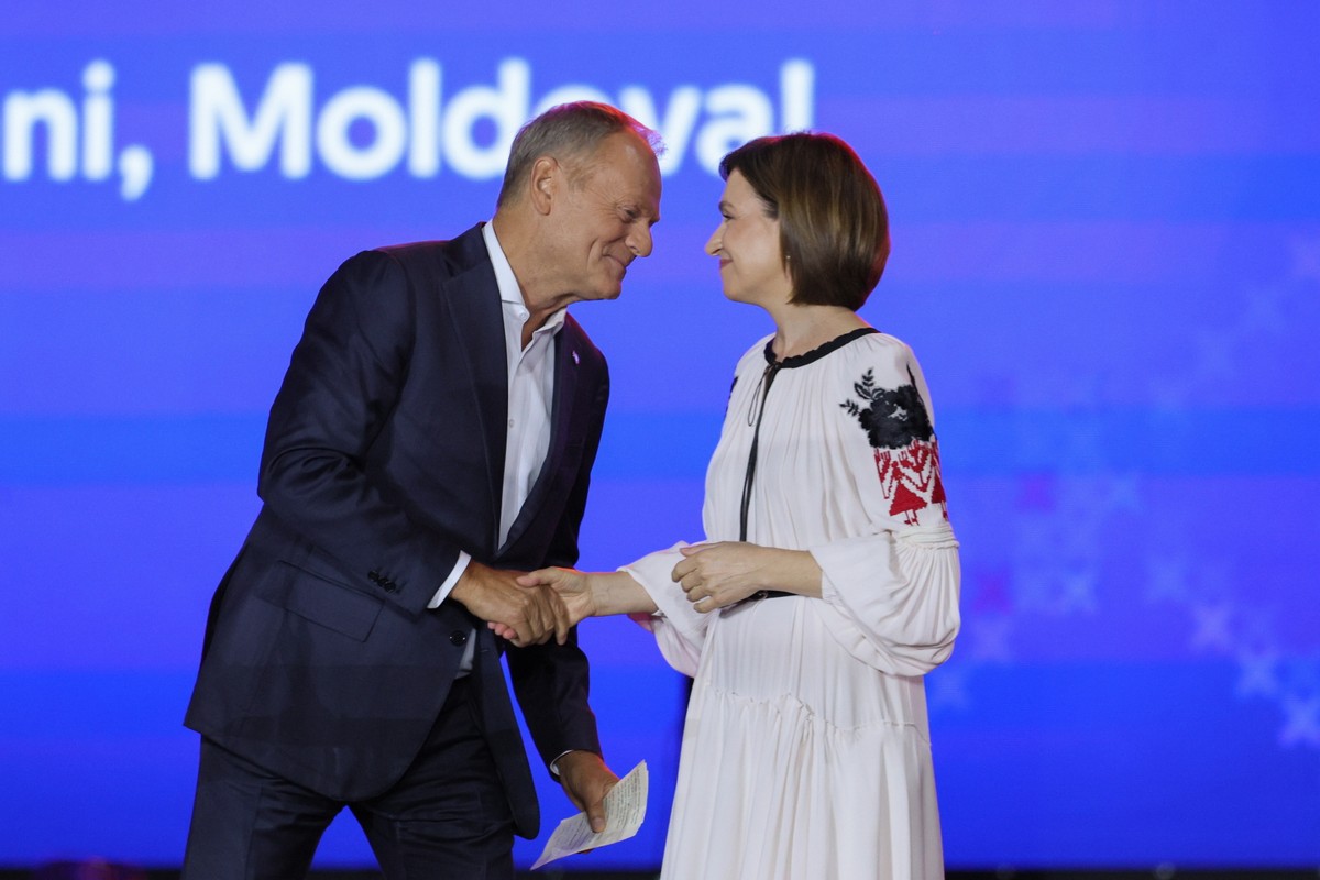 Premier Polski Donald Tusk i prezydent Mołdawii Maia Sandu podają sobie ręce podczas oficjalnego spotkania, stojąc na tle niebieskiego ekranu z napisem „Moldova”.