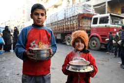 Children carry cooked meals provided by the UN through a partner NGO at al-Mashatiyeh neighborhood o