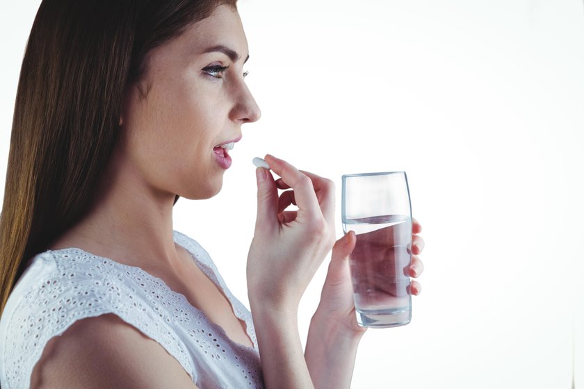 Pretty woman taking white pill on white background