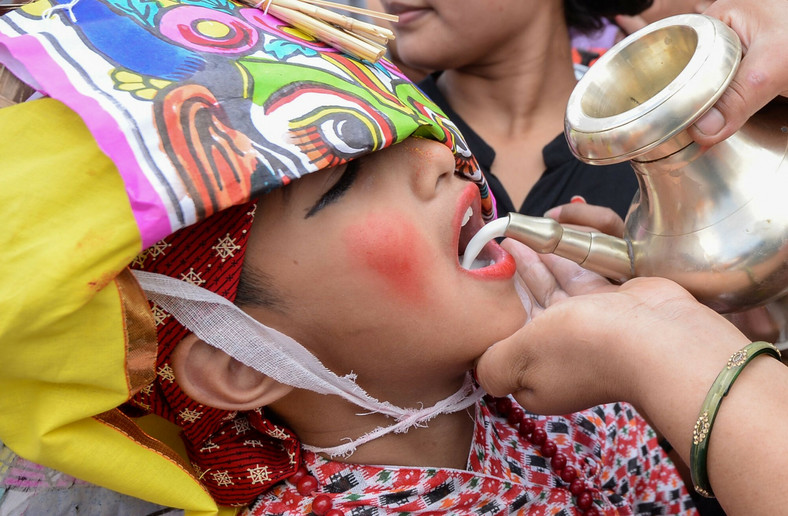 Nepalka wlewa mleko do ust chłopca podczas procesji na festiwal krów Gai Jatra w Katmandu, 16 sierpnia 2019 r.