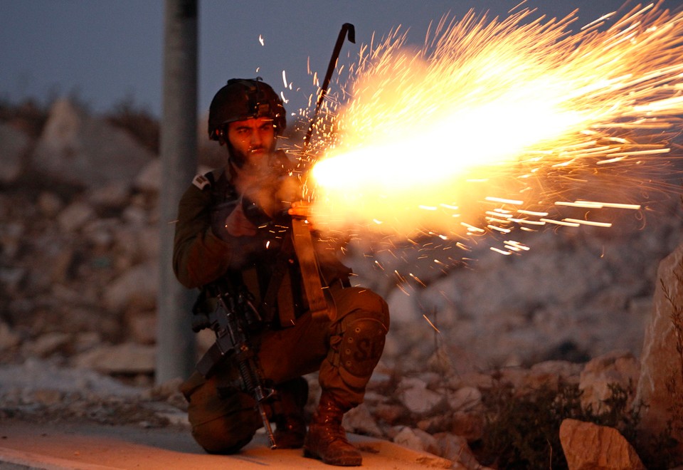 An Israeli soldier fires tear gas towards Palestinian youths throwing stones near Bethlehem