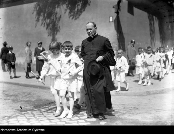 Ksiądz z dziećmi w strojach komunijnych idący ulicami Krakowa (1933).