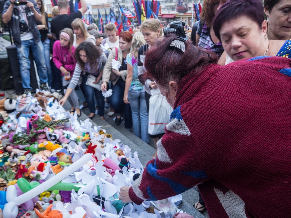 Ludzie układają zabawki pod zdjęciami poległych dzieci