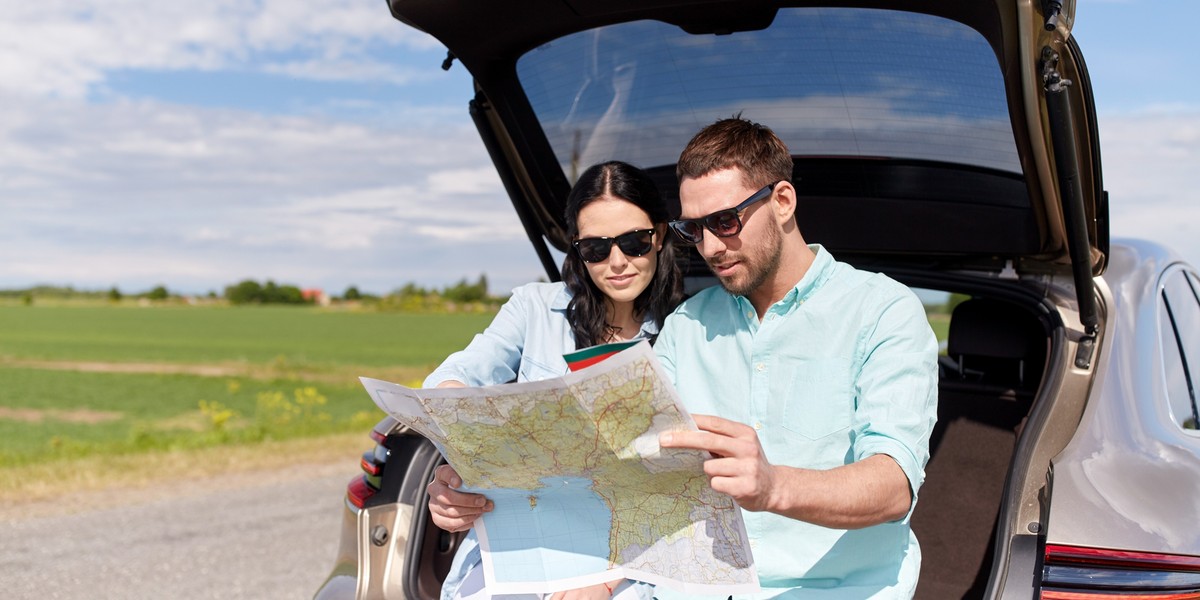 happy man and woman with road map driving in car