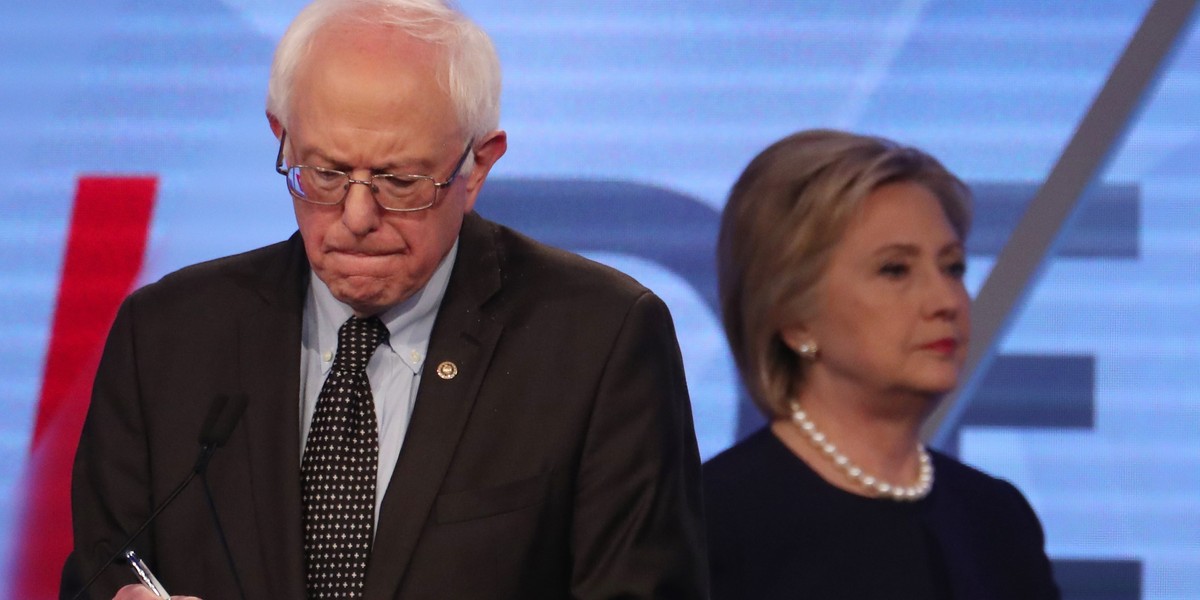 Democratic US presidential candidate Sen. Bernie Sanders writes on his notes as Hillary Clinton walks behind him to her podium during a commercial break at the Univision News and Washington Post Democratic presidential-candidates debate in Kendall, Florida, March 9, 2016.