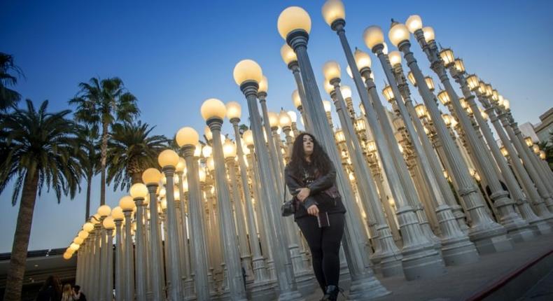 A young woman poses for a picture under Urban Light (2008), an assemblage of 202 antique street lamps by Chris Burden, one of LA's most photographed monuments