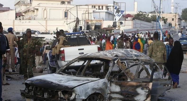A car suspected by the Somali police to have been used in a bomb attack is seen as residents gather to view the damage at the scene of the attack near Somali Youth League Hotel, known as SYL hotel, in Hamarweyne district in Mogadishu, February 27, 2016. At least nine people were killed when fighters from Somali Islamist group al Shabaab set off a car bomb at the gate of a popular park and near the hotel in the capital, sending a plume of smoke above the coastal city.  REUTERS/Feisal Omar  - RTS88AQ