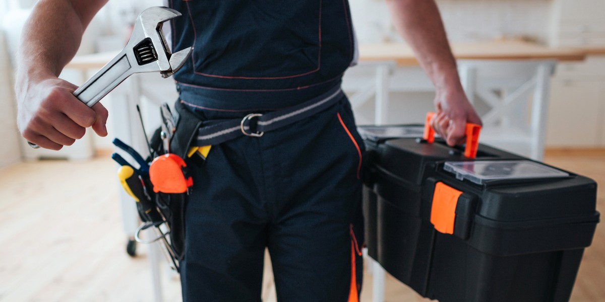 Cut view of handyman holding tool box and wrench in hands. He stand in kitchen. Guy wear special uni