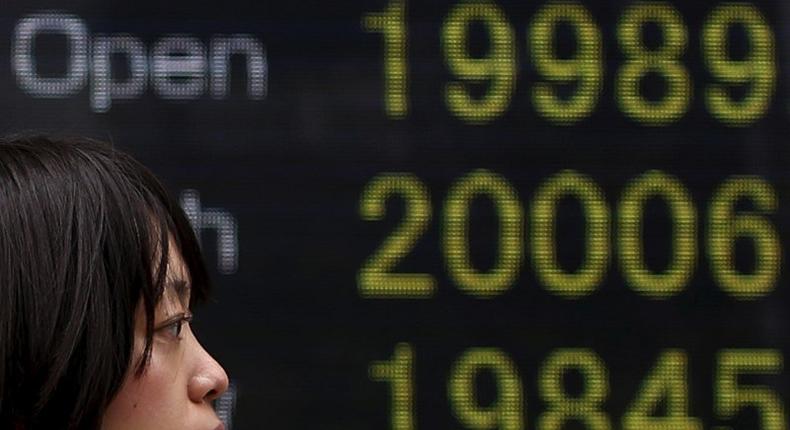 A pedestrian walks past an electronic board showing the Japan's Nikkei averages (from top current rate,daily high, and daily low) outside a brokerage in Tokyo April 10, 2015. REUTERS/Yuya Shino