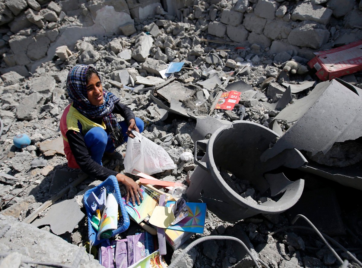 Palestyńska dziewczynka zbiera przybory szkolne w ruinach domu w Strefie Gazy