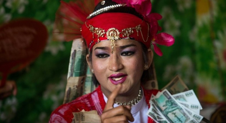 A medium wearing a red outfit and heavy make-up prepares to dance in honour of Myanmar's spirit guardian of drunkards and gamblers