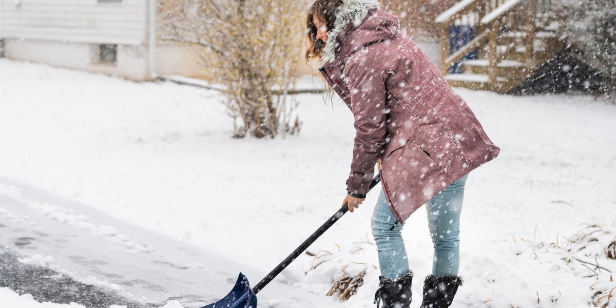 Young woman in winter coat cleaning shoveling driveway street from snow in heavy snowing snowstorm h