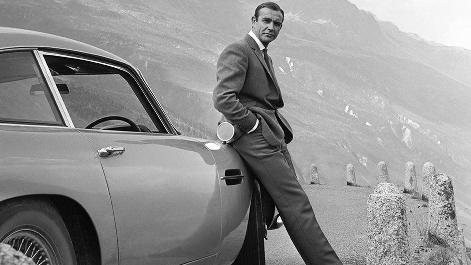 Sean Connery pozuje jako James Bond obok Astona Martina DB5 podczas sesji przed premierą filmu "Goldfinger" 