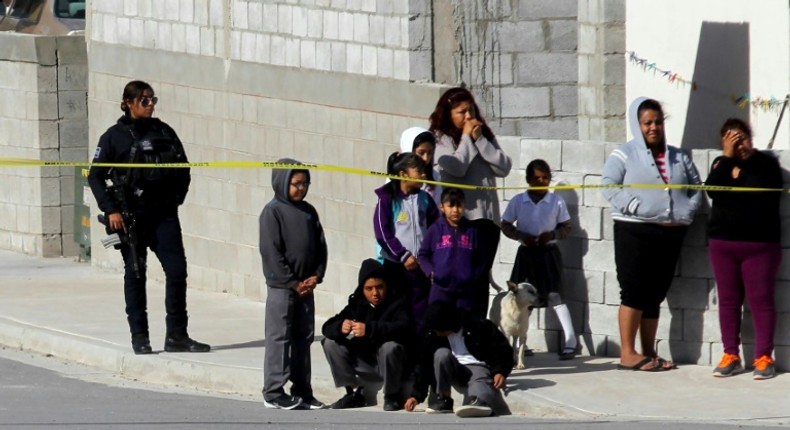 A police officer (L) and neighbors watch a house where five people were killed in Mexico's Ciudad Juarez on January 16, 2019 -- the country suffered a record 33,341 homicides in 2018