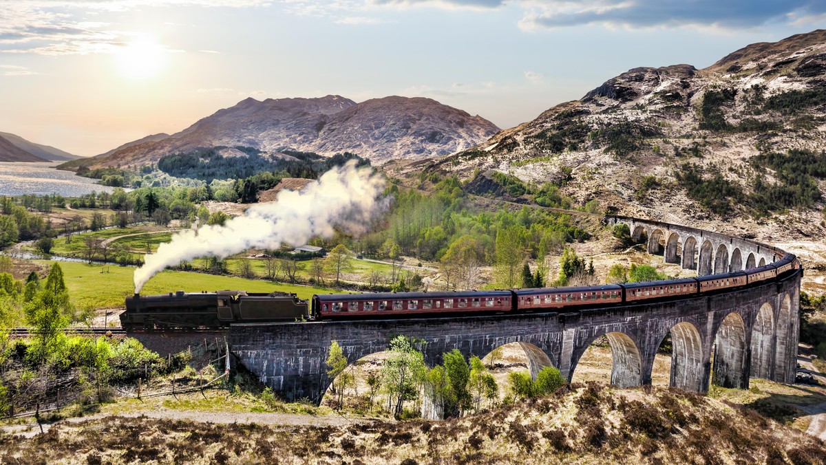 Glenfinnan Railway Viaduct in Scotland with the Jacobite steam train against sunset over lake