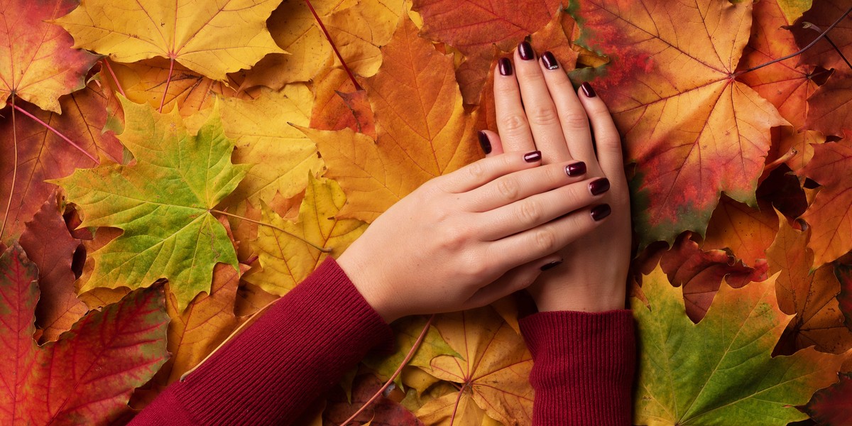 Female hand over autumn leaves background. Nail design concept.