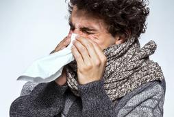 Ill young man with red nose, scarf and cap sneezing into handkerchief