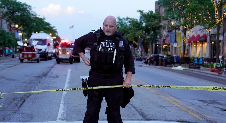 A police officer holds up police tape at the scene of a mass shooting at the Fourth of July parade in downtown Highland Park, a Chicago suburb, on Monday, July 4, 2022.