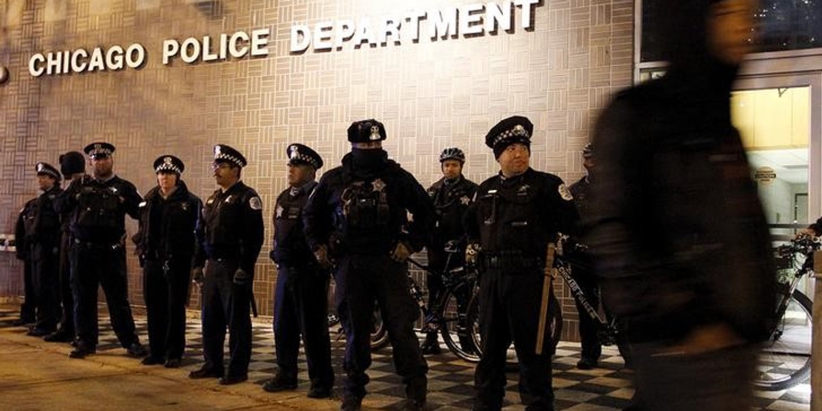 A protester walks past a line of police officers standing guard in front of the District 1 police headquarters in Chicago, Illinois November 24, 2015.