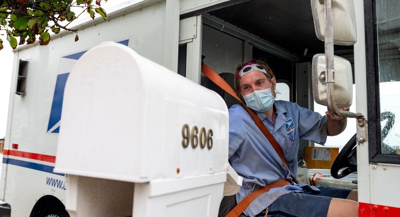 VENTNOR CITY, NEW JERSEY - AUGUST 13: A USPS worker wearing a mask puts envelopes in a mailbox while driving past as the state of New Jersey continues Stage 2 of re-opening following restrictions imposed to slow the spread of coronavirus on August 13, 2020 in Ventnor City, New Jersey. Stage 2, allows moderate-risk activities to resume which includes pools, youth day camps and certain sports practices.
