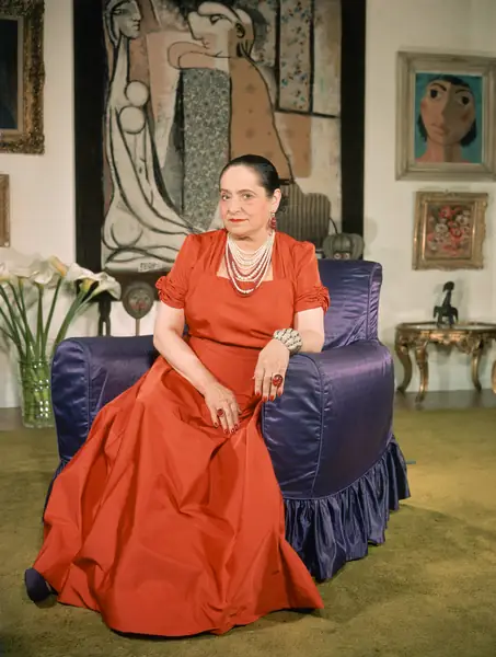  Helena Rubinstein siedząca na imperialnym fotelu w swoim mieszkaniu. z otaczającymi ją obiektami artystycznymi, m.in. Afrykańska maska na stole Blackamoor, wiktoriański posąg Blackamoor i obraz Dalego. (Zdjęcie: Herbert Gehr / The LIFE Images Collection via Getty Images / Getty Images)