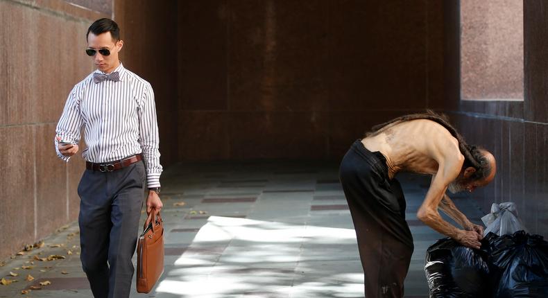 A man looks at his phone as he walks out of the courthouse past a man arranging his bags in Los Angeles, California July 8, 2014.