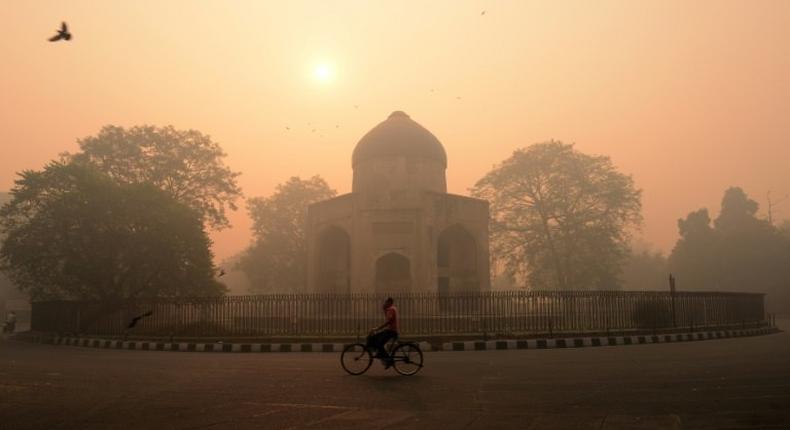 A cyclist rides along a street as smog envelops a monument in New Delhi on October 31, 2016, a day after the Diwali festival