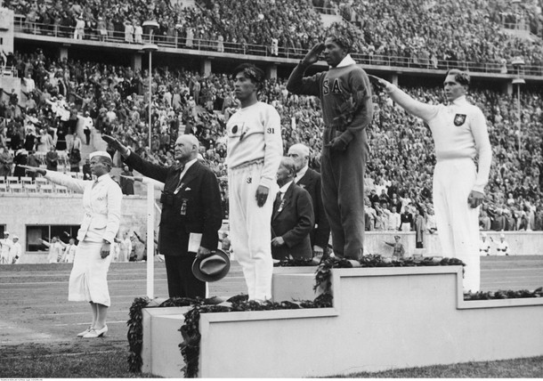 Letnie Igrzyska Olimpijskie w Berlinie. Uroczystość wręczenia medali zwycięzcom skoku w dal. Na podium stoją złoty medalista Jesse Owens (pośrodku), srebrny medalista Luz Long (z prawej) i brązowy medalista Naoto Tajima (z lewej), 1936 r. 