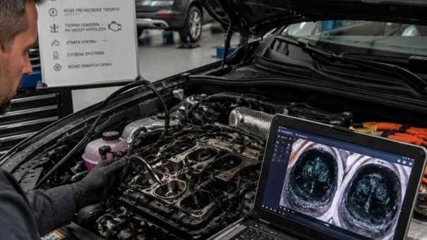 Detailný pohľad pod kapotu plug-in hybridného SUV v autorizovanom servise, kde mechanik s endoskopickou kamerou kontroluje sacie ventily spaľovacieho motora a na obrazovke notebooku sa zobrazujú čierne usadeniny – ilustrácia tichej degradácie motora pri vodičoch, ktorí auto pravidelne nenabíjajú a spaľovací motor v ňom pracuje s desiatkami studených štartov denne.