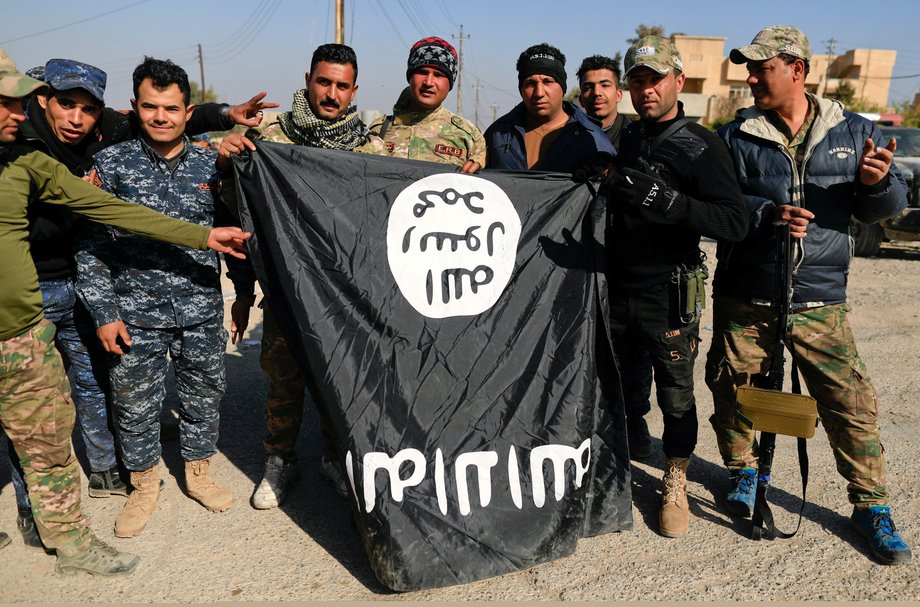 Iraqi security forces members pose with a seized ISIS flag after driving its militants out of Mosul's airport, southwest Mosul, Iraq, February 23, 2017.