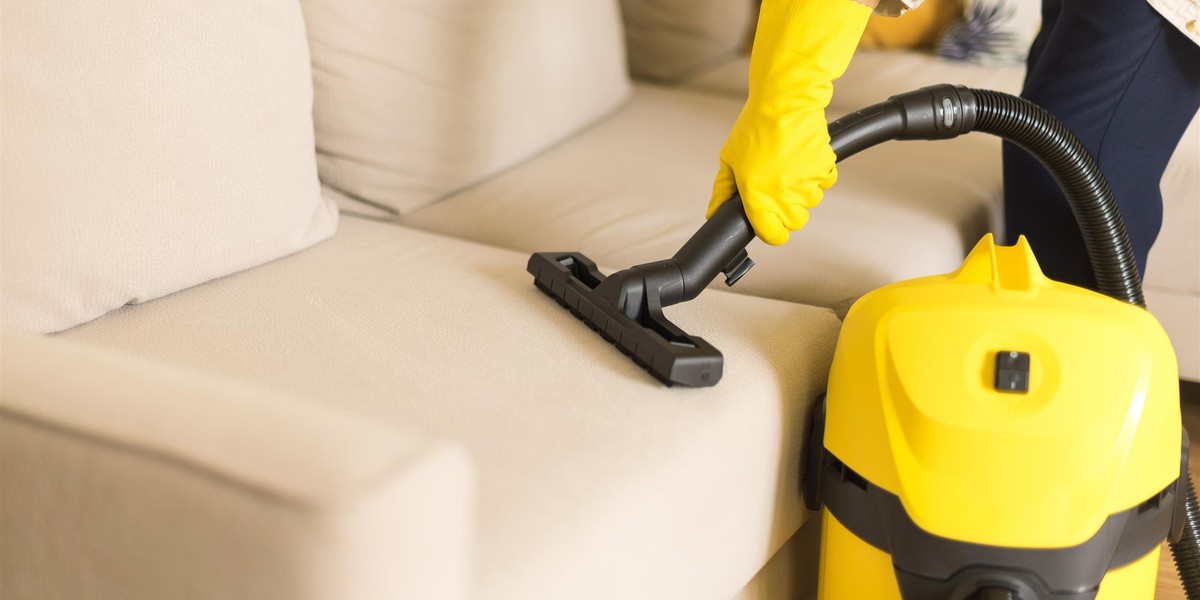 Woman cleaning sofa with yellow vacuum cleaner. Copy space. Clean concept