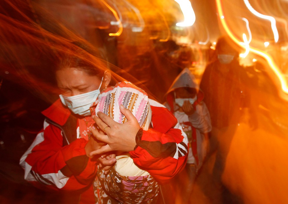 A woman covers her baby as she runs from ash falling from an erupting volcano at Kaliurang village in Sleman