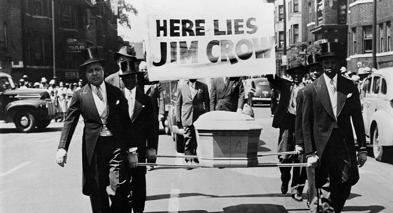 African American men wearing tuxedos carry a coffin and a Here Lies Jim Crow sign down the middle of a street as a demonstration against Jim Crow segregation laws.CORBIS/Corbis via Getty Images