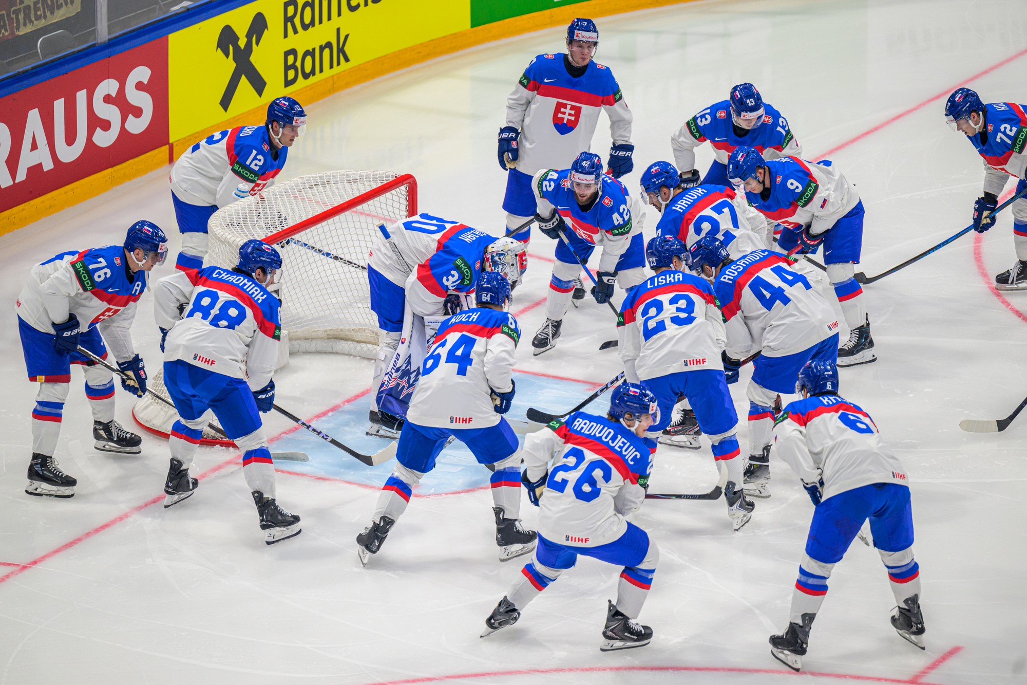 Slovenskí hokejisti stoja pred brankárom Adamom Gajanom. 