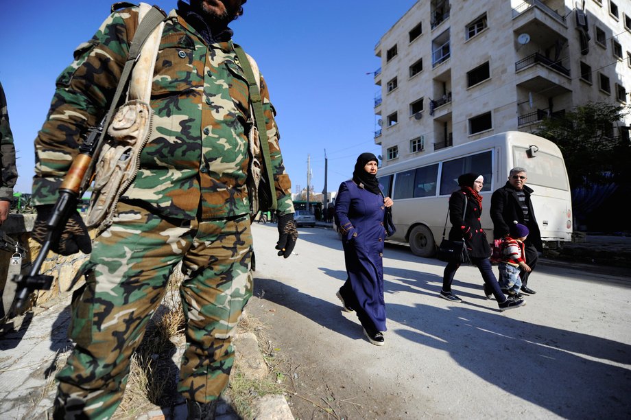 People who came back to inspect their homes walk near government soldiers in Aleppo.