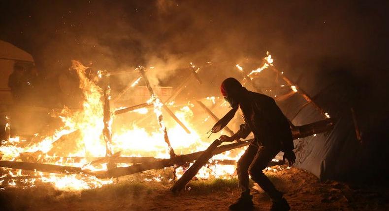 A migrant is seen in silhouette near flames from a burning makeshift shelter on the second day of the evacuation of migrants and their transfer to reception centers in France, as part of the dismantlement of the camp called the Jungle in Calais, France, October 25, 2016. 