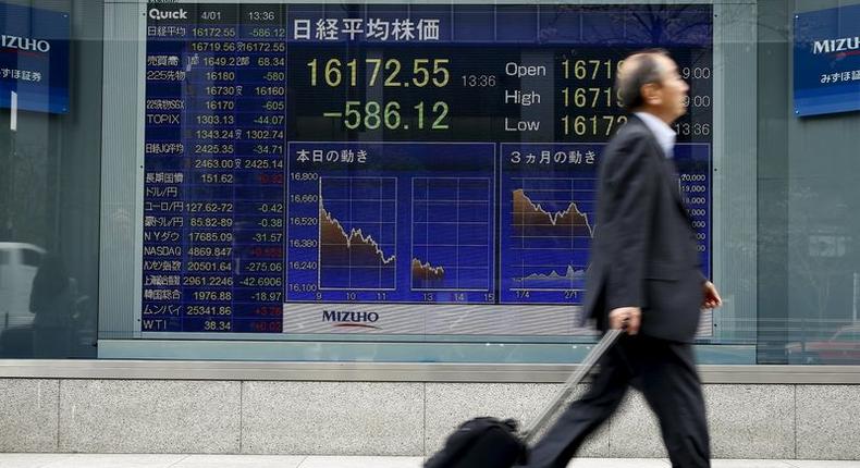 A man walks past an electronic board displaying the Nikkei average outside a brokerage in Tokyo, Japan, April 1, 2016. 