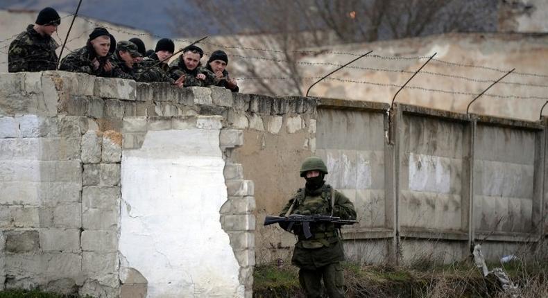 Ukrainian soldiers look on as an armed man, believed to be a Russian serviceman, stands guard at a Ukrainian military base in Perevalnoye in March 2014