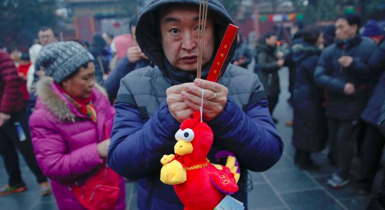 A man hold a rooster toy as people burn incense sticks and pray for good fortune at Yonghegong Lama Temple on the first day of the Lunar New Year of the Rooster in Beijing, China January 28, 2017.