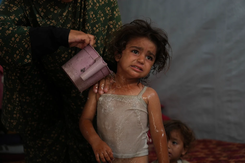 Rida Abu Hadajed (32) koristi vodu da ohladi svoju dvogodišnju ćerku Azhar u njihovom šatoru u kampu za raseljena lica u Kan Junisu, na jugu Pojasa Gaze