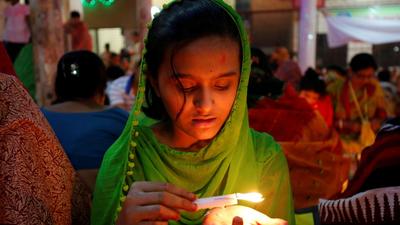 A girl pours melted hot wax on her hand from a candle as she sits on the floor of a temple to observe Rakher Upabash for the last day, in Dhaka, Bangladesh