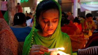 A girl pours melted hot wax on her hand from a candle as she sits on the floor of a temple to observe Rakher Upabash for the last day, in Dhaka, Bangladesh