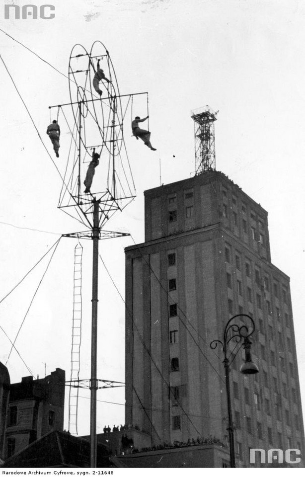 Wyczyny akrobatyczne na wysokości 36m wykonywane na kole z rur przy pl. Napoleona. W tle budynek Prudentialu z eksperymentalną anteną telewizyjną na dachu (1942 r.)