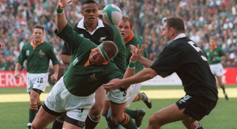 Springbok Kobus Wiese (C) loses the ball as he falls between All Blacks Jonah Lomu (behind) and Robin Brooke (R) during the 1995 Rugby World Cup final  in Johannesburg