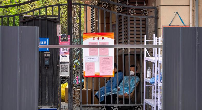 Men wearing protective clothing sit at the entrance of a residential building that has been surrounded by metal barricades as part of COVID-19 controls in Beijing, China, on June 14, 2022.Mark Schiefelbein/AP