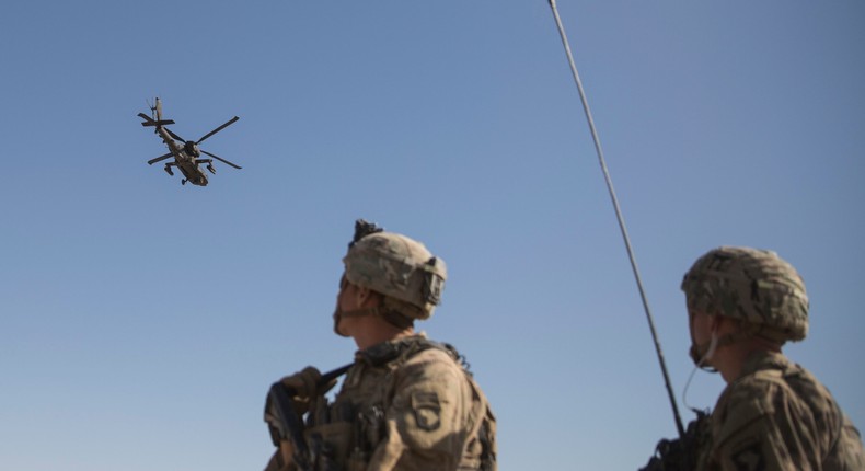 An AH-64 Apache attack helicopter provides security from above while CH-47 Chinooks drop off supplies to US Soldiers at Bost Airfield, Afghanistan on June 10, 2017.US Marine Corps photo by Sgt. Justin T. Updegraff, Operation Resolute Support via AP