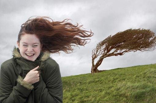 Young woman standing on windswept hill, smiling, eyes closed